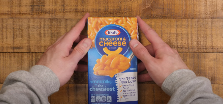 hand holding a box of kraft macaroni and cheese on a wooden table