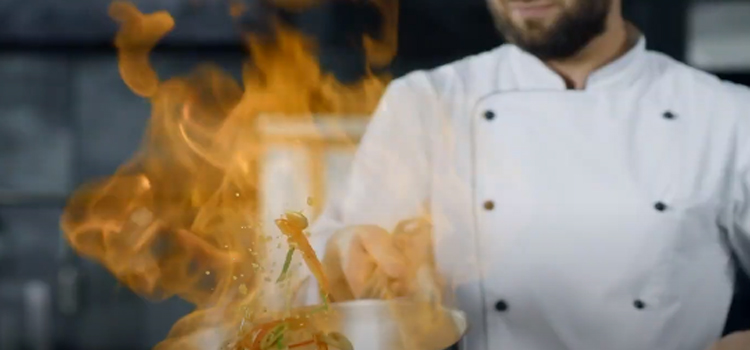 Chef holding pan performing flambe on a dish