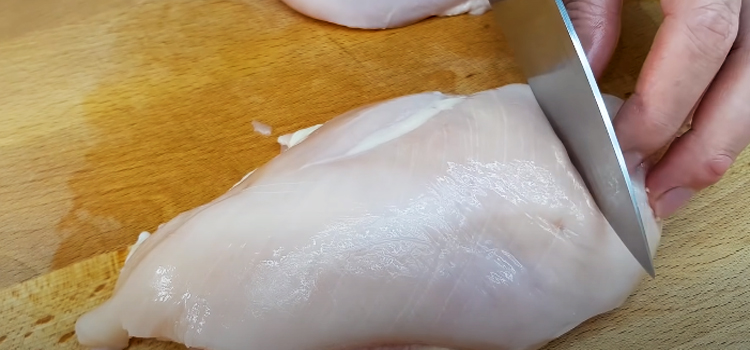 slicing chicken breast on a wooden chopping board